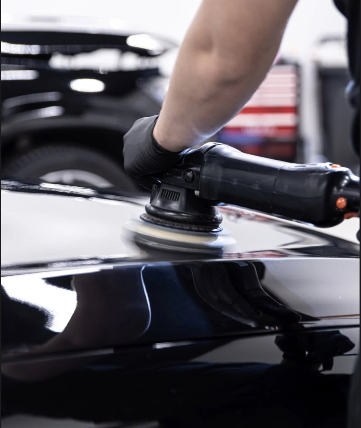 A detailer machine-polishing the deep-gloss black paint of a car, reflections mirror-sharp in the panel.